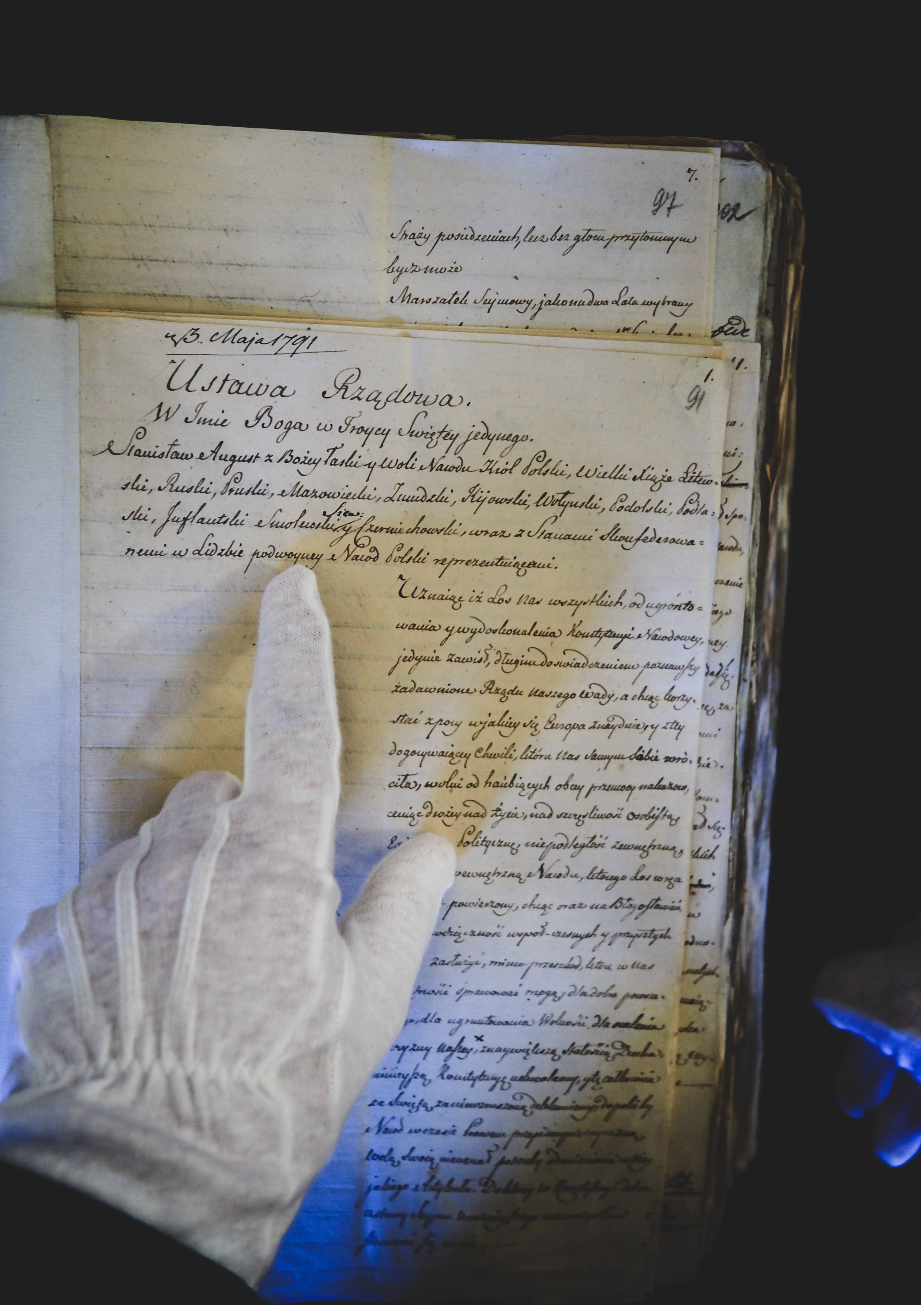Osoba w białej rękawiczce wskazuje na zapisy we fragmencie Konstytucji 3 Maja.
