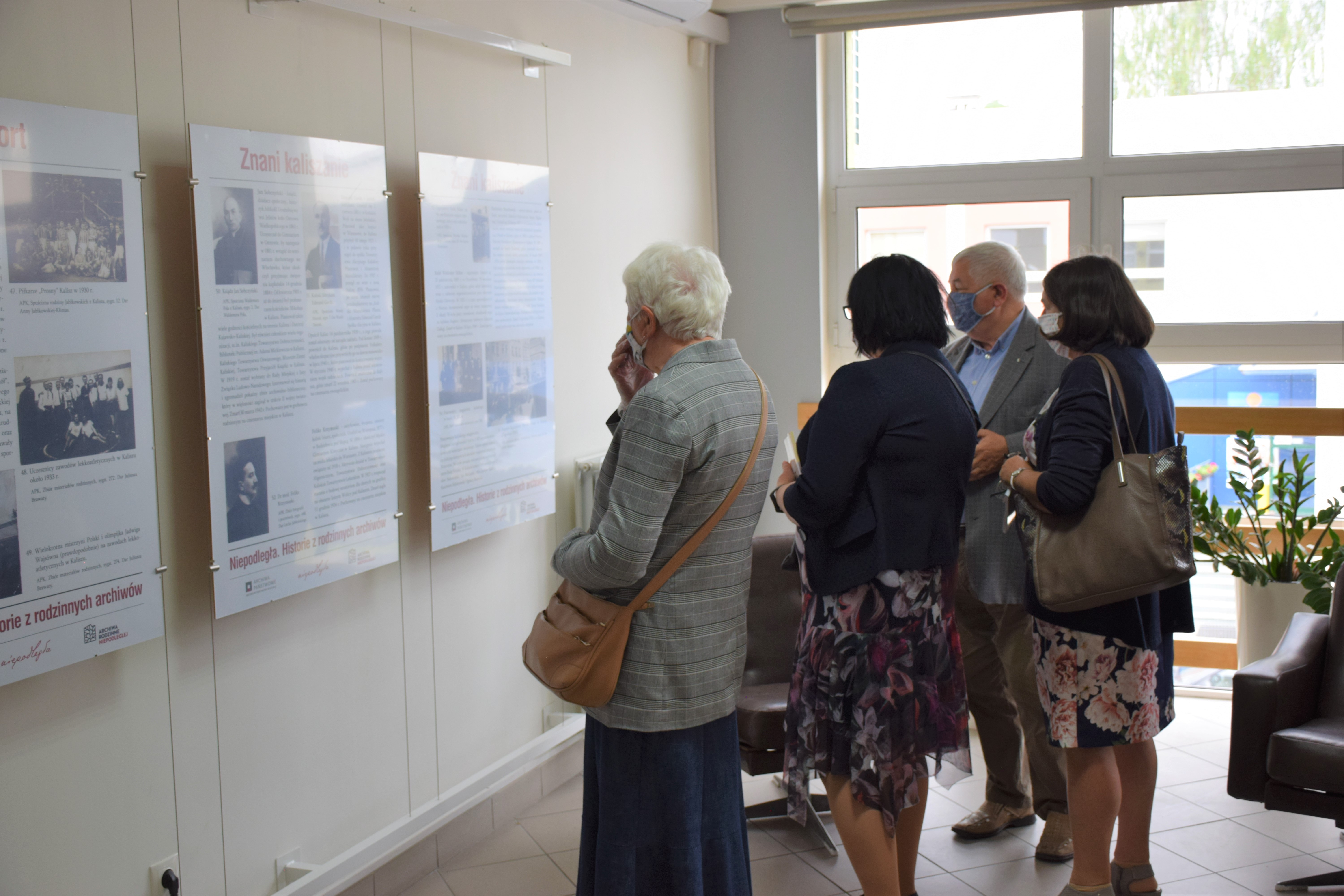 Grupa gości wydarzenia ogląda zainstalowane przy ścianie plansze wystawy.