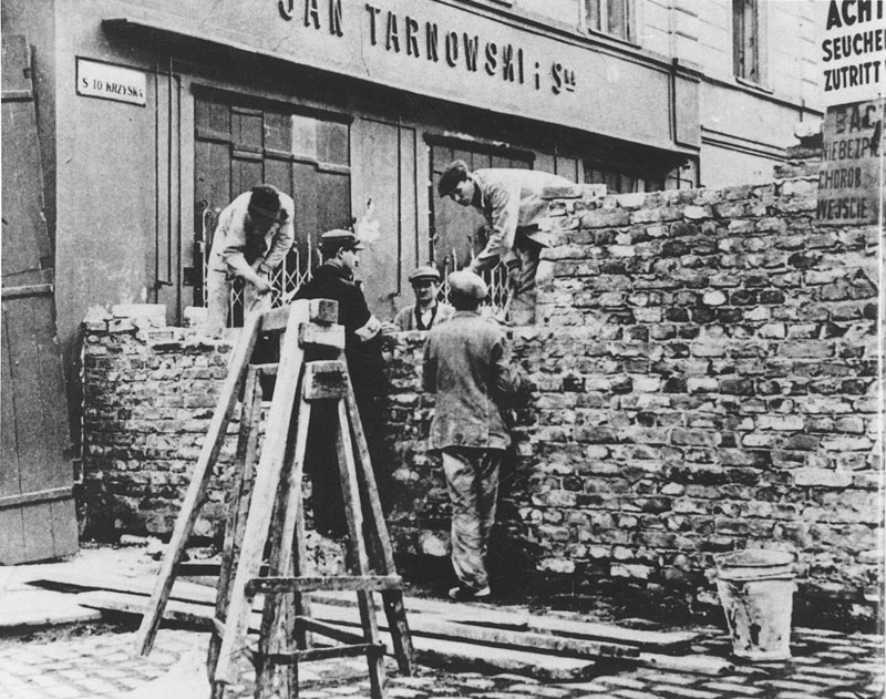 Budowa muru getta warszawskiego. 5 mężczyzn buduje mur.