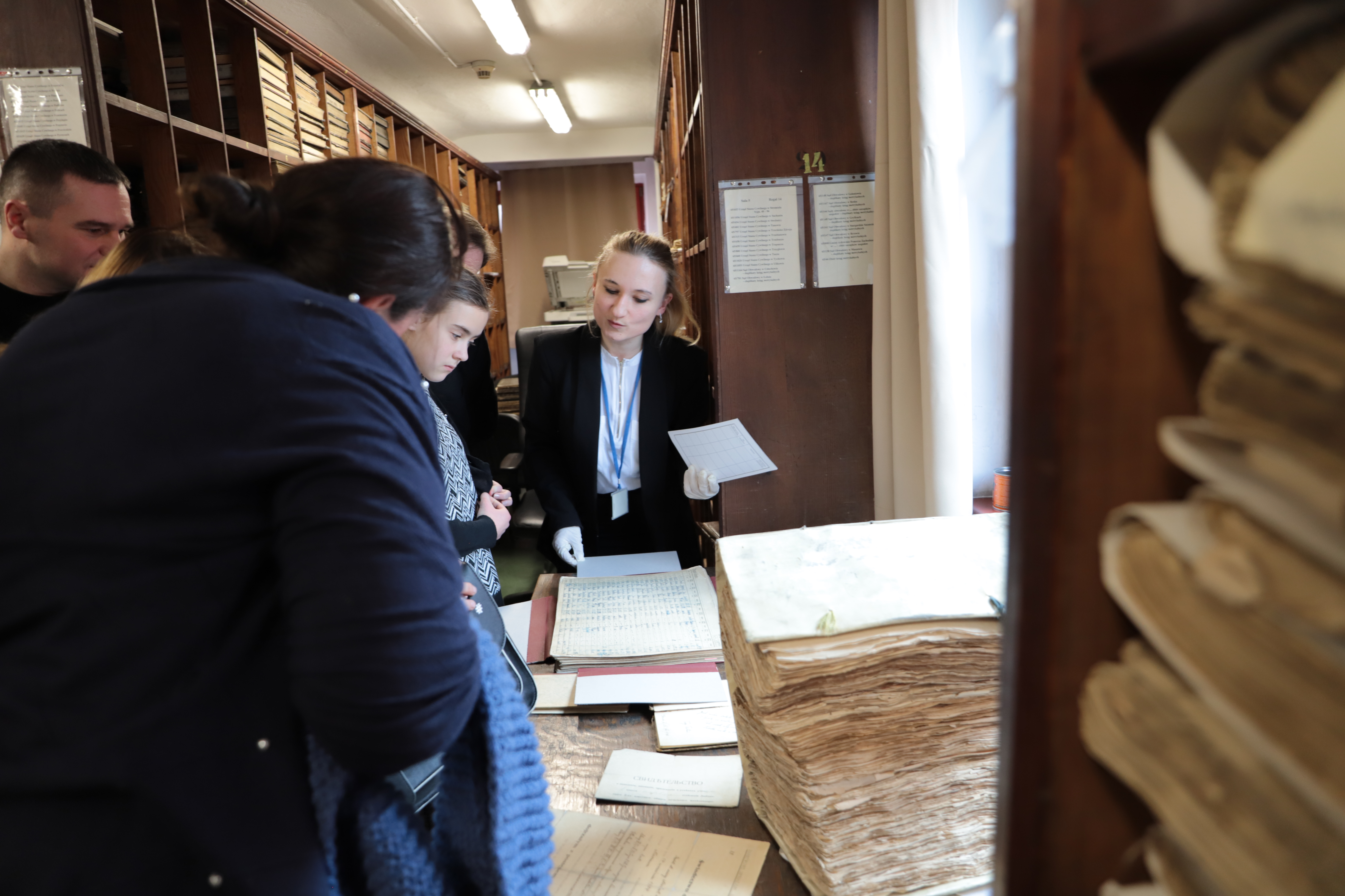 Archiwistka pokazuje gościom materiały archiwalne przechowywane w magazynie. 