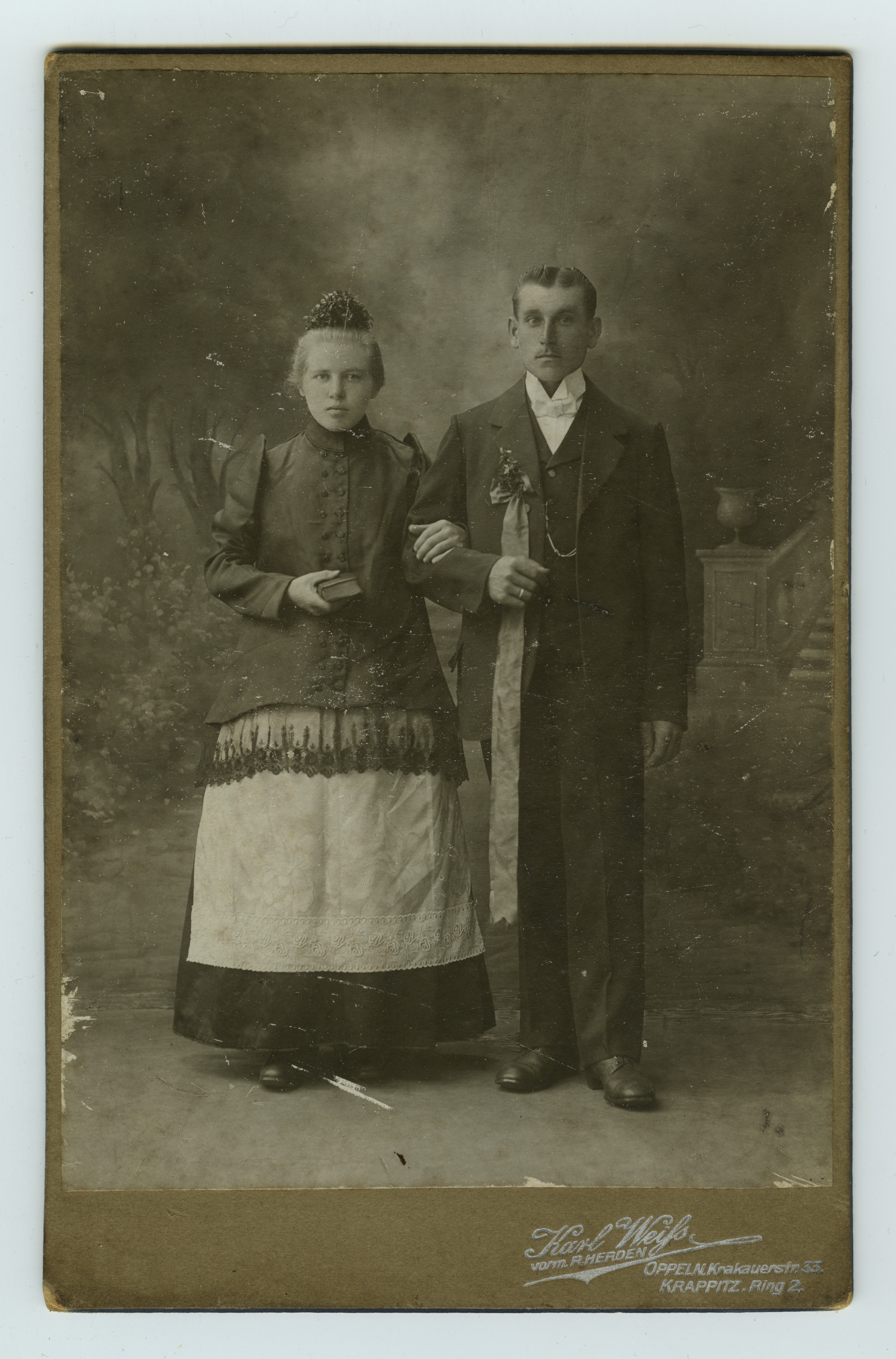 Elegancko ubrani kobieta i mężczyzna, kobieta obejmuje mężczyznę pod ramię.