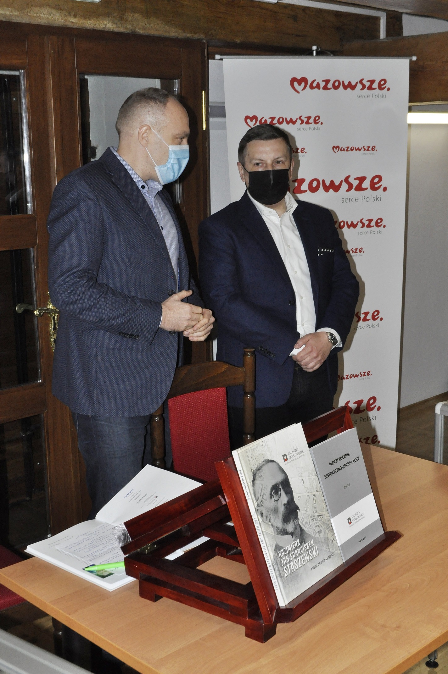 Piotr Gryszpanowicz i dyrektor Piekarski stoją przy stoliku na którym wystawione są dwie publikacje.