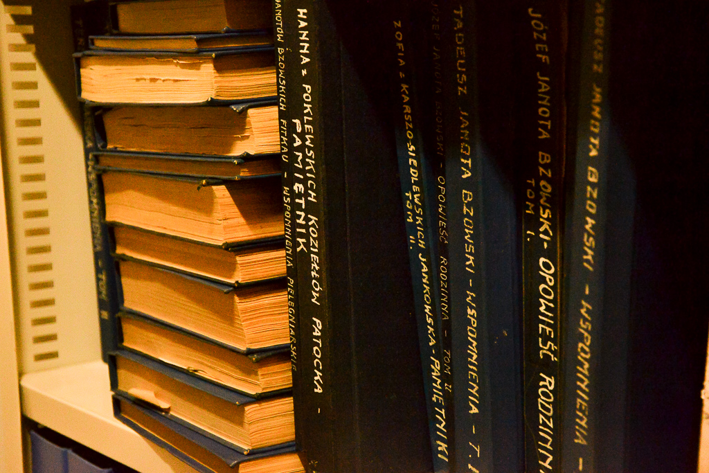 Półka z księgami część stoi część leży jedne na drugich. 