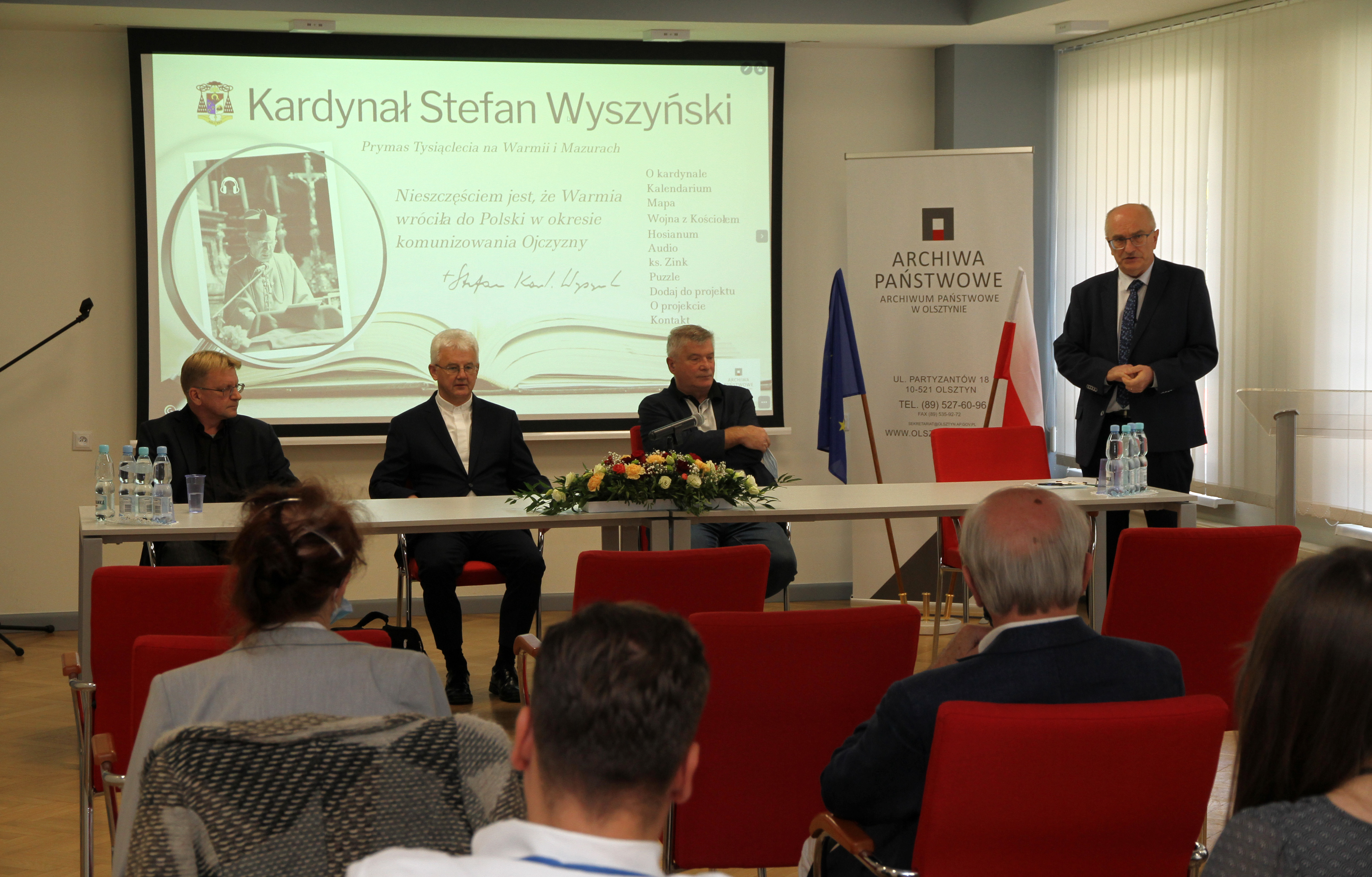 Trzech gości siedzi za stołem konferencyjnym, obok stoi i przemawia dyrektor Archiwum prof. Norbert Kasparek.