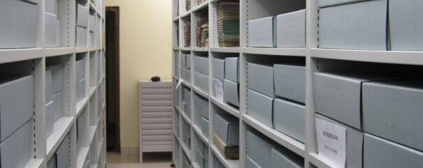Regały archiwalne. Na półkach leżą szare pudła archiwalne.