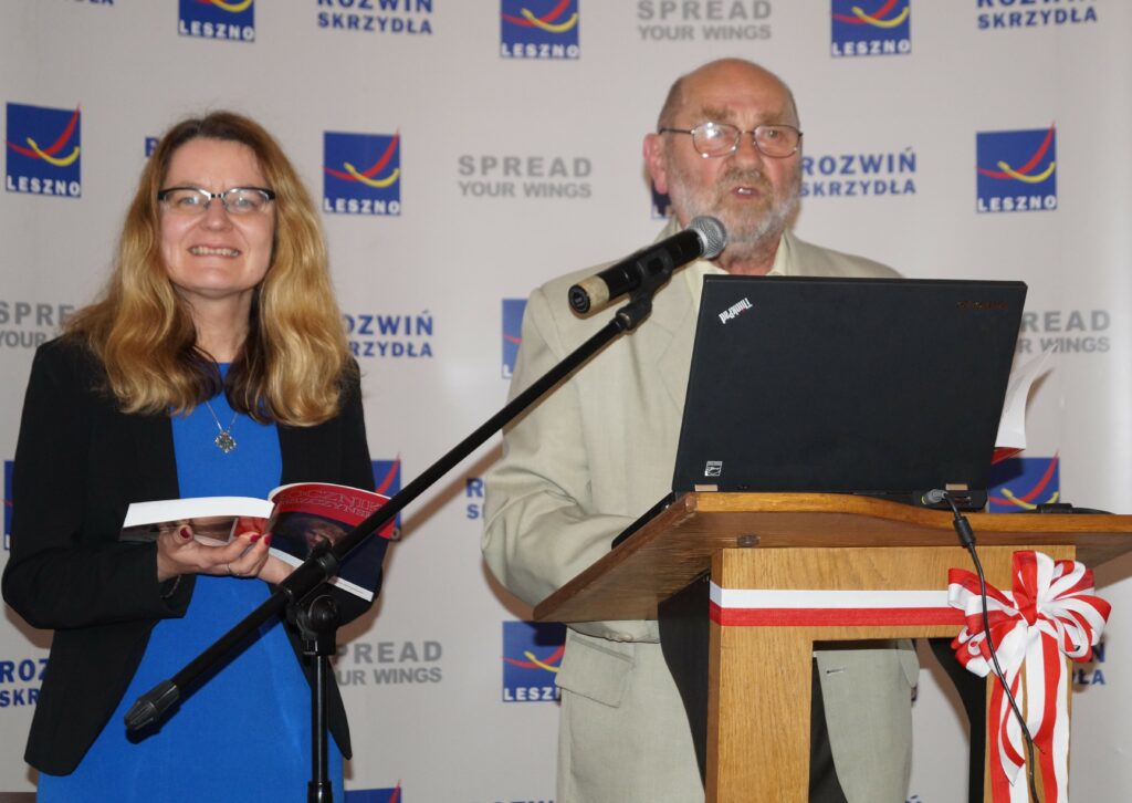 Dwie osoby stoją za mównicą. Kobieta trzyma w ręku książkę. 