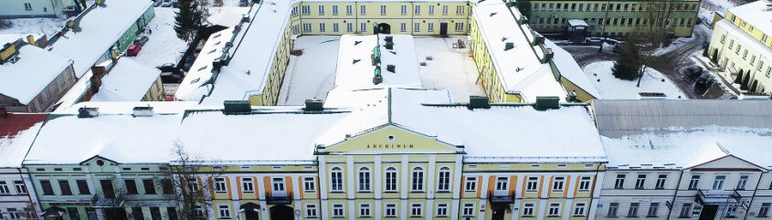 Budynek archiwum z żółto-biało-pomarańczową elewacją, widziany z loty ptaka, na dachu i na ulicy leży śnieg.