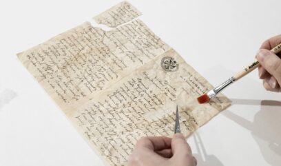 Konserwator podkleja kartę rękopisu za pomocą bibułki, pędzelka z klejem i pęsety.