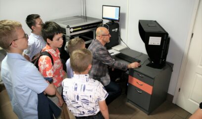 Pracownik archiwum przy komputerze ze skanerem. Dookoła grupa dzieci.