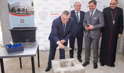 Wicepremier Gliński symbolicznie wrzuca szpachlą beton we fragment muru.