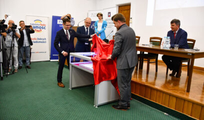 Dyrektorzy Żygawski Krawczuk i Pietrzyk odsłaniają czerwoną tkaninę ze szklanej gabloty z aktem.