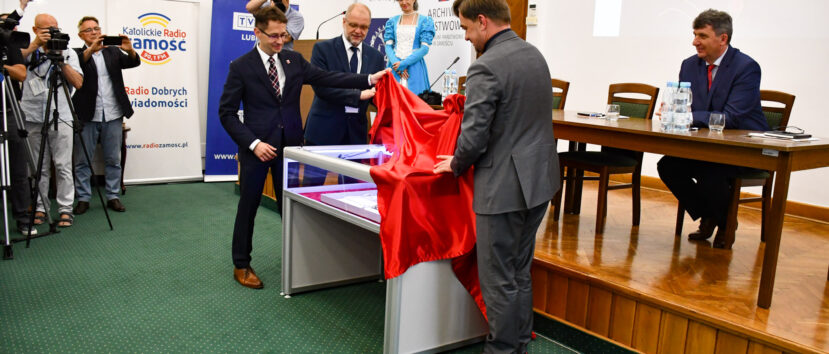 Dyrektorzy Żygawski Krawczuk i Pietrzyk odsłaniają czerwoną tkaninę ze szklanej gabloty z aktem.