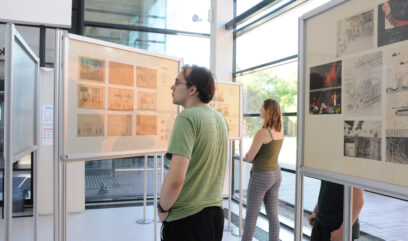 Plansze w wystawą stoją w sali wystawienniczej. Trzy osoby oglądają wystawę.