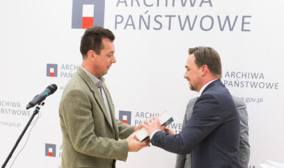 Zdobywca wyróżnienia odbiera książkę z rąk Naczelnego Dyrektora Archiwów Państwowych Pawła Pietrzyka.