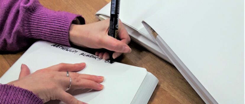 Kobieta wpisuje czarnym markerem nazwę kolekcji na białej teczce.