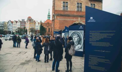 Goście oglądają plansze wystawy. W tle stare miasto w Gdańsku.