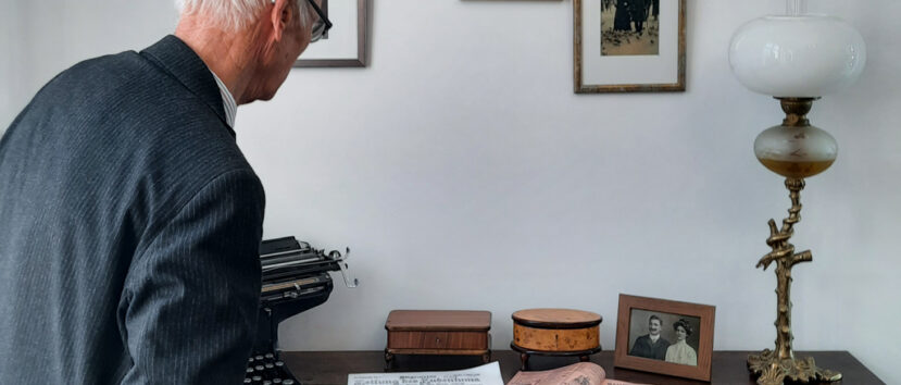 Gość wydarzenia przygląda się eksponatowi – biurku z epoki z rozłożoną na nim prasą, lampą, dwiema drewnianymi szkatułkami, zdjęciem w ramce i maszyną do pisania.