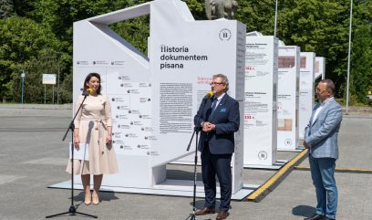 Trzy osoby stoją przed wystawą. Dyrektor Katarzyna Królczyk i mężczyzna stoją przy mikrofonach.