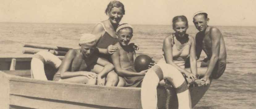 Stara fotografia. 5 osób siedzi na łódce na plaży.