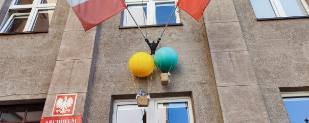 Wejście do budynku. Obok wejście wiszą polski flagi oraz instalacje balonów z wystawy.