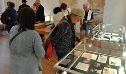 Sala wystawowa. 10 osób ogląda wyłożone w szklanych gablotach i na stolikach materiały archiwalne.