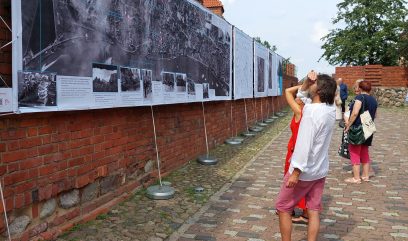Grupa ludzi ogląda wystawę wywieszoną na murach Barbakanu.