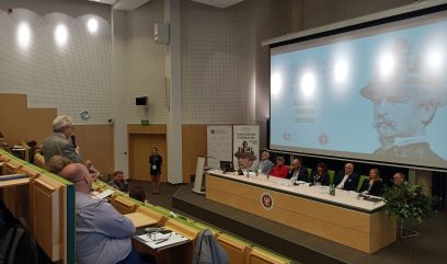 Za stołem konferencyjnym na scenie siedzi 7 panelistów. Uczestnik z sali zadaje pytanie.