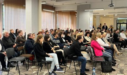 Goście siedzą w rzędach na sali konferencyjnej.