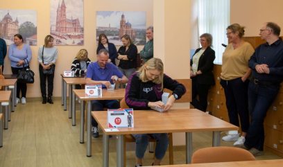 Zawodnicy siedzą przy stolikach i składają pudła archiwalne.