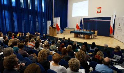 Sala wykładowa. Tłum na sali. Na scenie za pulpitem prelegentka.