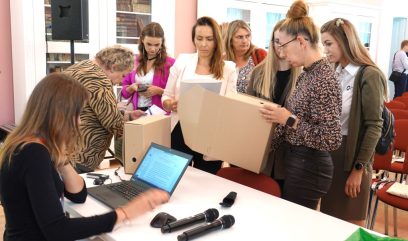 7 osób stoi wokół stolika i ogląda pudła archiwalne. Jedna osoba siedzi przy laptopie przy stoliku.