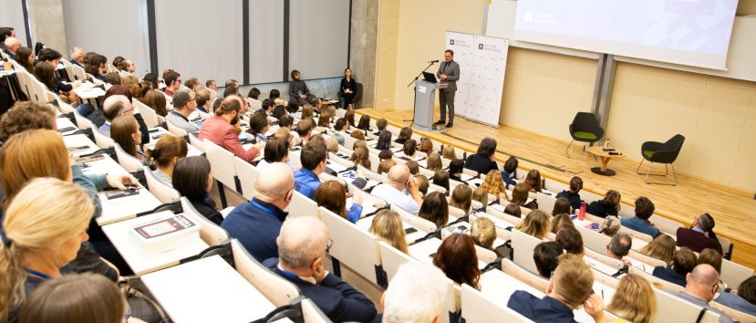 Aula wykładowa. Dyrektor Pietrzyk przemawia do mikrofonu. Za nim rollupy z logo Archiwa Państwowe. Przed nim siedzi publiczność.