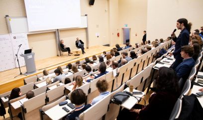 Kamila Pawełczyk-Dura i dr Paweł Pietrzyk siedzą na scenie na fotelach przy stoliku. Publiczność siedzi na auli. Mężczyzna z publiczności zadaje pytanie.