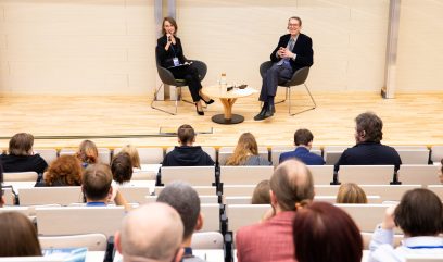 Kamila Pawełczyk-Dura i dr Paweł Pietrzyk siedzą na scenie na fotelach przy stoliku. Publiczność siedzi na auli.