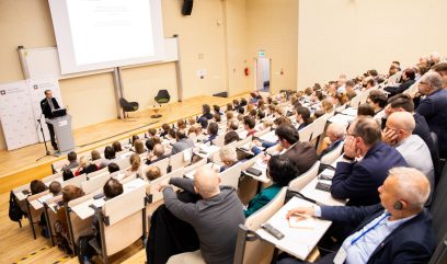 Aula wykładowa. Geoffrey Yeo na scenie przemawia do mikrofonu. Za nim rollupy z logo Archiwa Państwowe.