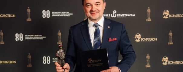 Naczelny Dyrektor Archiwów Państwowych dr Paweł Pietrzyk pozuje na ściance ze statuetką Bohaterona.