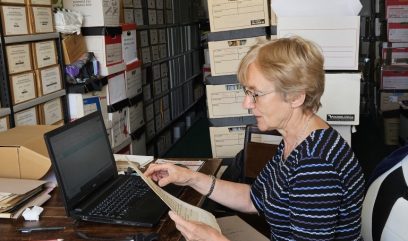 Anna Laszuk siedzi przy stoliku i przegląda dokumenty. Na stoliku stoi otwarty laptop.