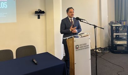 Sala konferencyjna. Dyrektor Pietrzyk przemawia zza mównicy.