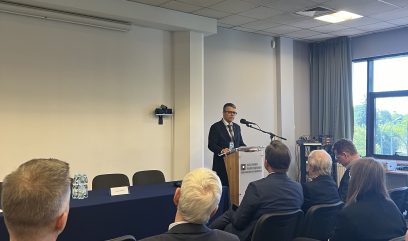 Sala konferencyjna. Dyrektor Olczak przemawia zza mównicy.
