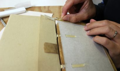 Konserwatorka łączy paskami materiału oprawę z grzbietem księgi.