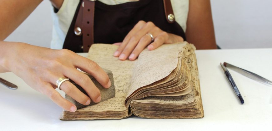 Konserwatorka czyści karty księgi gąbeczką.