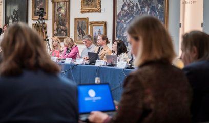 Eksperci i ekspertki siedzą w sali za stołami.