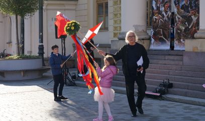 Olgierd Łukaszewicz i dwójka dzieci stykają się trzymanymi przez siebie chorągwiami.