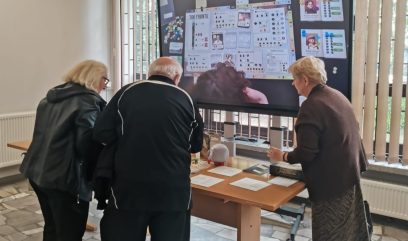 3 osoby nachylają się nad stolikiem z prezentacją gry.