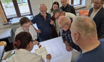 7 osób ogląda prezentowany przez 2 konserwatorki proces konserwacji dokumentu.