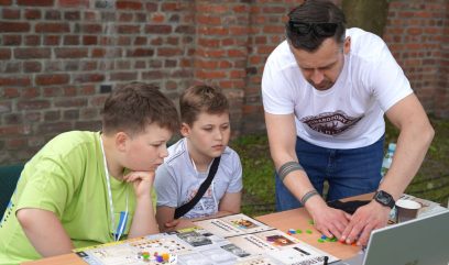 Dwóch chłopców i archiwista grają w grę planszową.