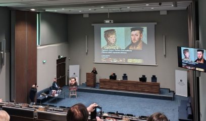 Sala konferencyjna, za stołem i pulpitem prelegenci, na sali siedzi publiczność, na ekranie wyświetlana jest prezentacja nt. Zygmunta Augusta i Barbary Radziwiłłówny.