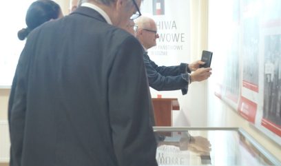 Goście oglądaj materiały wyłożone gablotach. Jedna osoba robi zdjęcie planszom wystawy wiszącym na ścianie.