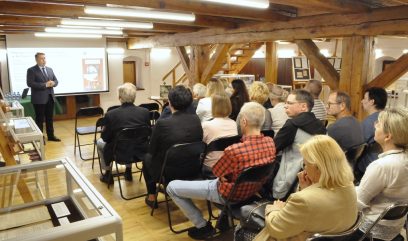 Sala konferencyjna. Publiczność siedzi na Sali. Prelegent stoi i przemawia.