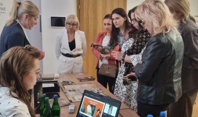 Grupa osób stoi dookoła stolika na którym prezentowana jest gra.